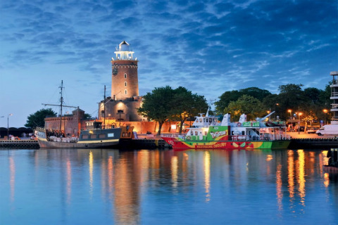 Abendstimmung am Hafen mit beleuchtetem Leuchtturm und Booten in Kołobrzeg nahe Ferienhaus.