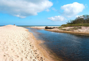 Billede af en bred sandstrand med en lille flod og grøn vegetation nær sommerhytter i Mielno, Danmark.