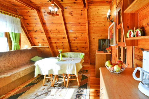 Indretning af træhytte med spiseplads, sofa, grønne gardiner og naturligt lys ved Sommerhus Osieki, Danmark.