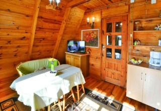 Sommerhusets hyggelige træinteriør med spisebord, sofa, tv, og køkkenfaciliteter i Osieki, Danmark.