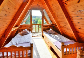 Indvendigt af et hyggeligt sommerhus med to enkeltsenge i et A-formet træloft med balkonudsigt.
