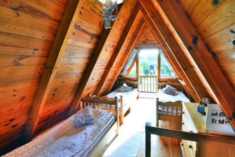 Zolderkamer met houten wanden en drie eenpersoonsbedden in een zomerhuisje in Osieki, Denemarken, met uitzicht.