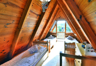 Zolderkamer met houten panelen en drie aparte bedden in een zomerhuis in Osieki, Denemarken, met buitenzicht.