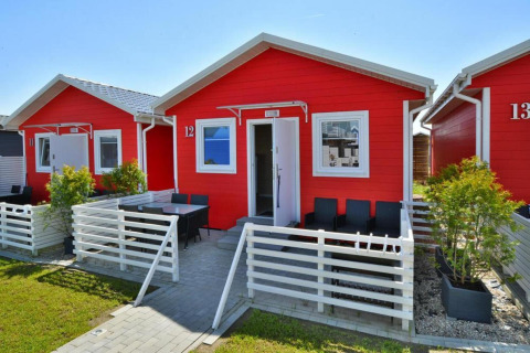 Eengezins rode vakantiehuisjes in Sarbinowo met witte hekken, buitenterras en groene planten.