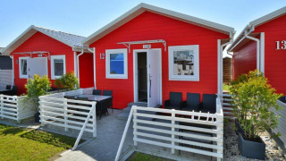 Eengezins rode vakantiehuisjes in Sarbinowo met witte hekken, buitenterras en groene planten.