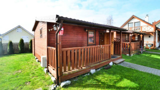 Enkeltliggende træhytte på 30 m2 i Ustronie Morskie med veranda og grøn have under blå himmel.