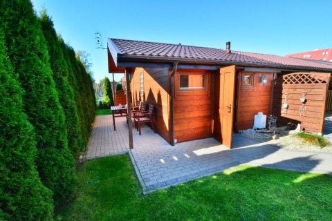 Houten chalet met open deur en terras, omgeven door groene hagen, bij Older year-round cottage TYPE A Ustronie Morskie.