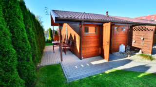 Chalet in legno con porta aperta e patio, circondato da siepi verdi, presso Older year-round cottage TYPE A Ustronie Morskie.