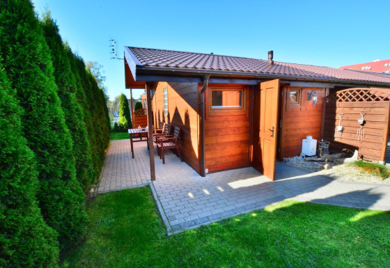 Houten hut met open deur en terras, omringd door groene hagen bij Older year-round cottage TYPE A Ustronie Morskie.