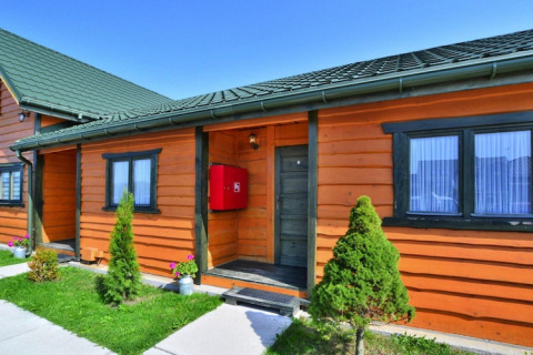 Casa di legno con tetto verde, Holiday cottages Sarbinowo, giardino curato e cielo sereno.