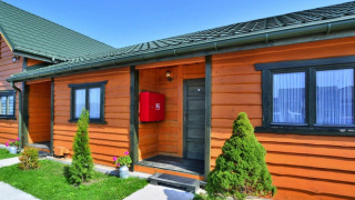 Houten huisje met groen dak en tuin, Holiday cottages Sarbinowo, blauwe lucht en zonnige dag.