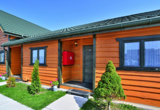 Houten huisje met groen dak en tuin, Holiday cottages Sarbinowo, blauwe lucht en zonnige dag.