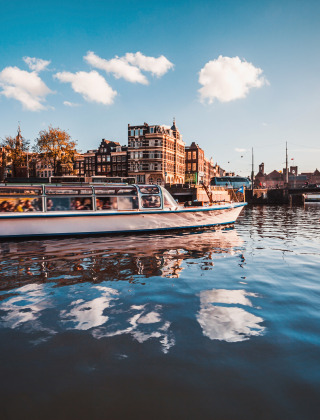 Bootsfahrt auf einem Kanal in einer europäischen Stadt mit alten Gebäuden und blauem Himmel im Hintergrund.