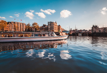Paseo en barco por un canal en una ciudad europea con edificios históricos bajo un cielo azul y nubes blancas.