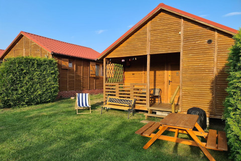 Single-storey cottages in Jarosławiec featuring wooden cabins, red roofs, outdoor chairs, and a picnic table.