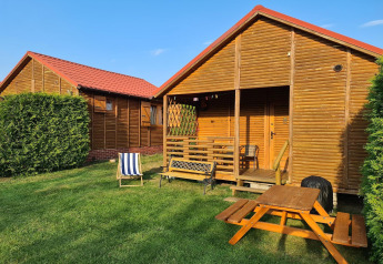 Single-storey cottages in Jarosławiec featuring wooden cabins, red roofs, outdoor chairs, and a picnic table.