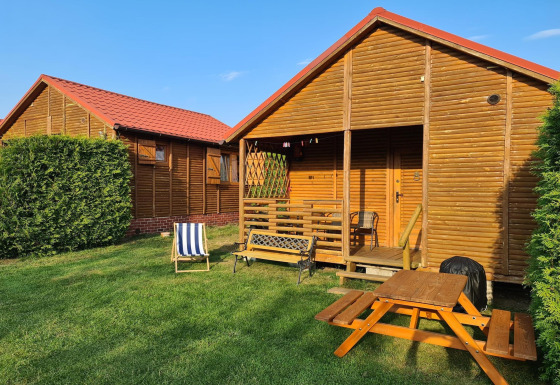 Single-storey cottages in Jarosławiec featuring wooden cabins, red roofs, outdoor chairs, and a picnic table.