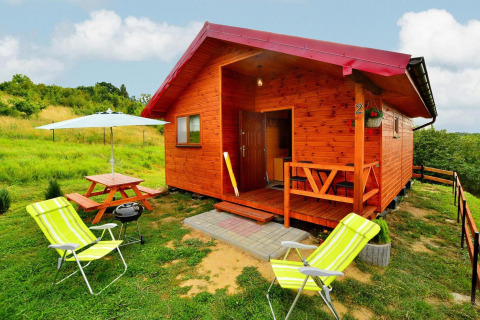 Charming wooden cabin Domki letniskowe Rusinowo with porch, picnic table, lawn, and sun loungers.