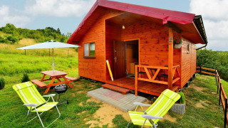 Houten chalet Domki letniskowe Rusinowo met veranda, picknickbank, gras en ligstoelen buiten.
