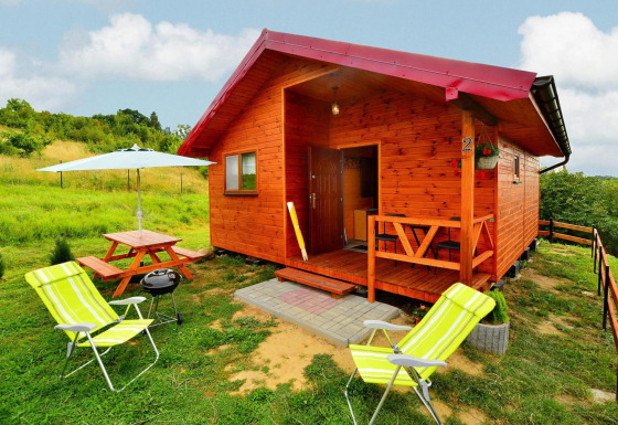 Charming wooden cabin Domki letniskowe Rusinowo with porch, picnic table, lawn, and sun loungers.