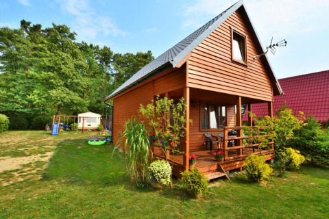 Houten lodge Domek 5-osobowy Jarosławiec met veranda, tuin en speelplek in een groene omgeving.