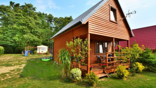 Houten lodge Domek 5-osobowy Jarosławiec met veranda, tuin en speelplek in een groene omgeving.