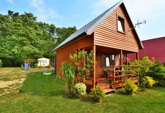 Casa in legno Domek 5-osobowy Jarosławiec con veranda, giardino e area giochi immersa nel verde.