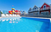 Udendørs swimmingpool med liggestole, farverige hytter og et legepladsområde på Single-storey holiday cottages Sarbinowo i Danmark.