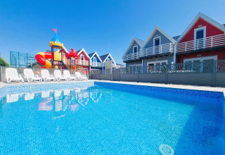 Piscina al aire libre con tumbonas, casas de colores y área de juegos en Single-storey holiday cottages Sarbinowo, Dinamarca.