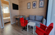 Bright lodge living room with grey sofa, red chairs, dining table, wall art, and bedroom entrance.