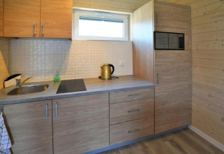 Moderne houten keuken met gootsteen, kookplaat, waterkoker en magnetron in lodge Sarbinowo, Denemarken.