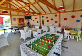 Sala de juegos en lodge con futbolín, mesa de ping pong, mesas, sillas y área infantil colorida.