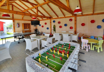 Sala de juegos en lodge con futbolín, mesa de ping pong, mesas, sillas y área infantil colorida.