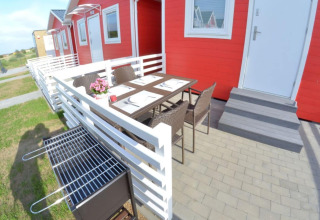Buitenterras met eettafel, stoelen en barbecue voor rode vakantiehuisjes in Sarbinowo, Denemarken.