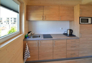 Moderne kleine Küchenzeile mit Holzschränken, Spüle, Kochfeld und Wasserkocher in einer Ferienhütte.