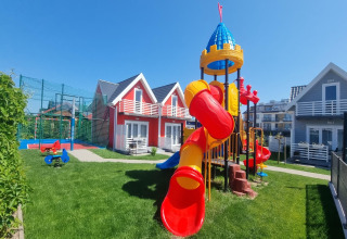 Kleurrijke speeltuin bij gelijkvloerse vakantiewoningen in Sarbinowo, met gras en blauwe lucht.