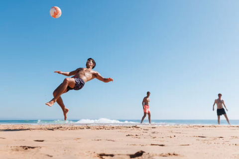 Trois hommes jouent au football sur la plage près de Single-storey holiday cottages Sarbinowo au Danemark.