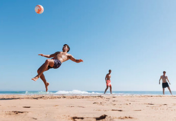 Drei Männer spielen Strandfußball vor den Single-storey holiday cottages Sarbinowo an Dänemarks Küste.