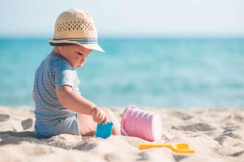Een jong kind met zonnenhoedje speelt met emmertjes en speelgoed op het strand in Sarbinowo, Denemarken.