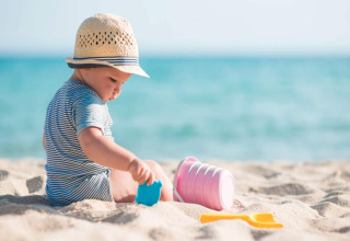 Ein kleines Kind mit Strohhut spielt mit Eimern und Spielzeug am Sandstrand in Sarbinowo, Dänemark.