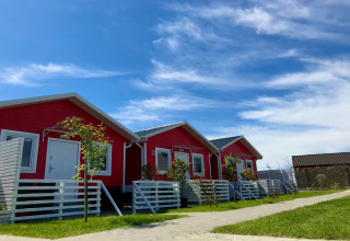 Rangée de chalets de vacances rouges de plain-pied avec clôtures blanches sous un ciel bleu lumineux.