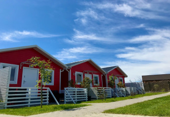 Reihe roter einstöckiger Ferienhäuser mit weißen Zäunen und grünem Rasen unter blauem Himmel.