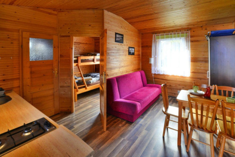 Interior of a wooden cabin with a purple sofa, kitchen, dining table, and bunk bed in Ustronie Morskie.