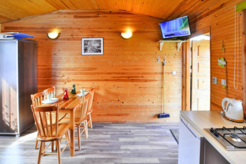 Interior of a wooden cottage with dining table, chairs, kitchenette, and wall-mounted TV in Ustronie Morskie.