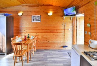 Interieur van een houten huisje met eettafel, stoelen, kitchenette en wand-tv in Ustronie Morskie.