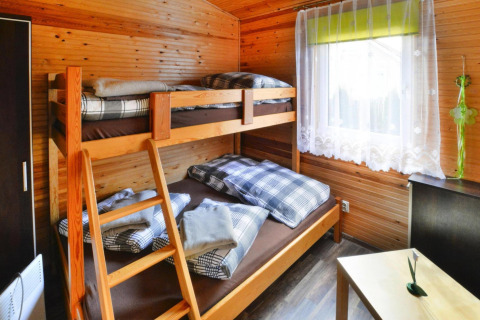 Knusse houten kamer met stapelbed, geruit beddengoed, zonnig raam en een klein tafeltje.