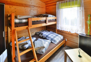 Knusse houten kamer met stapelbed, geruit beddengoed, zonnig raam en een klein tafeltje.
