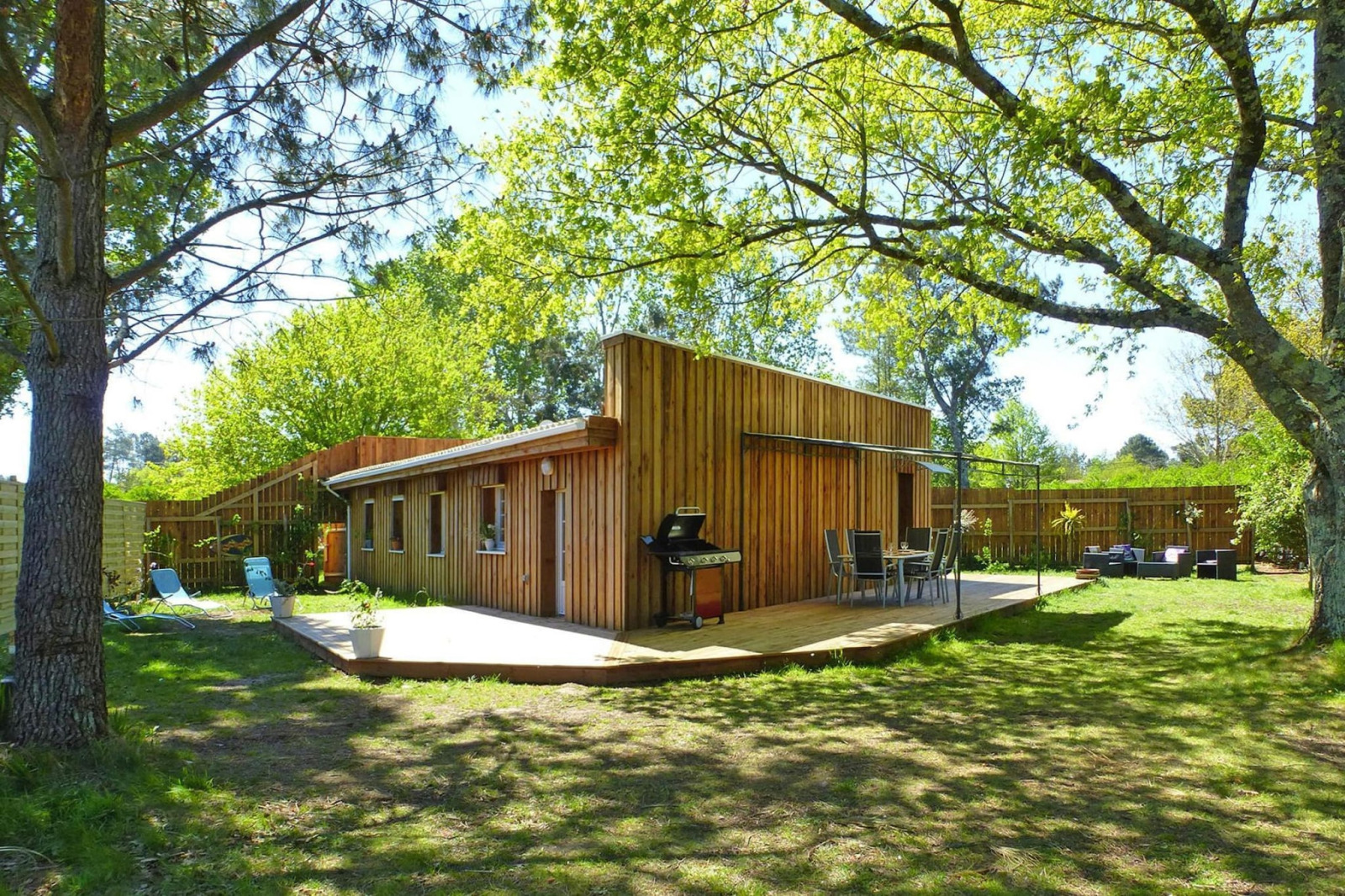 Vakantiehuis Le Porge, houten lodge met terras, barbecue en tuinmeubilair in een zonnige tuin.