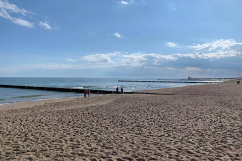 Beach view from a cottage in Ustronie Morskie, Denmark, showing sea, piers and a sandy shore.