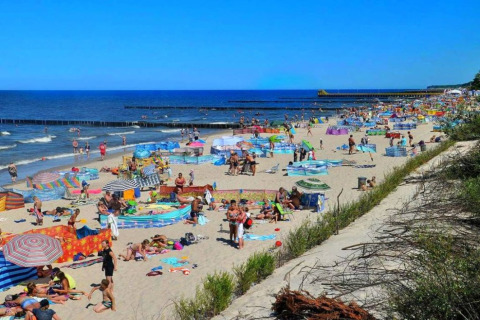 Drukke strand in Ustronie Morskie met kleurrijke windschermen, zonaanbidders en gezinnen aan zee.